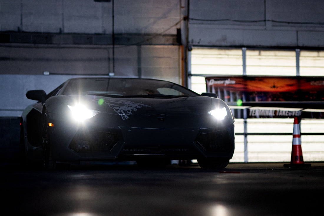 A Lamborghini Aventador blazes its headlights head on inside the hangar with the Terminal Takeover event banner glowing behind it.