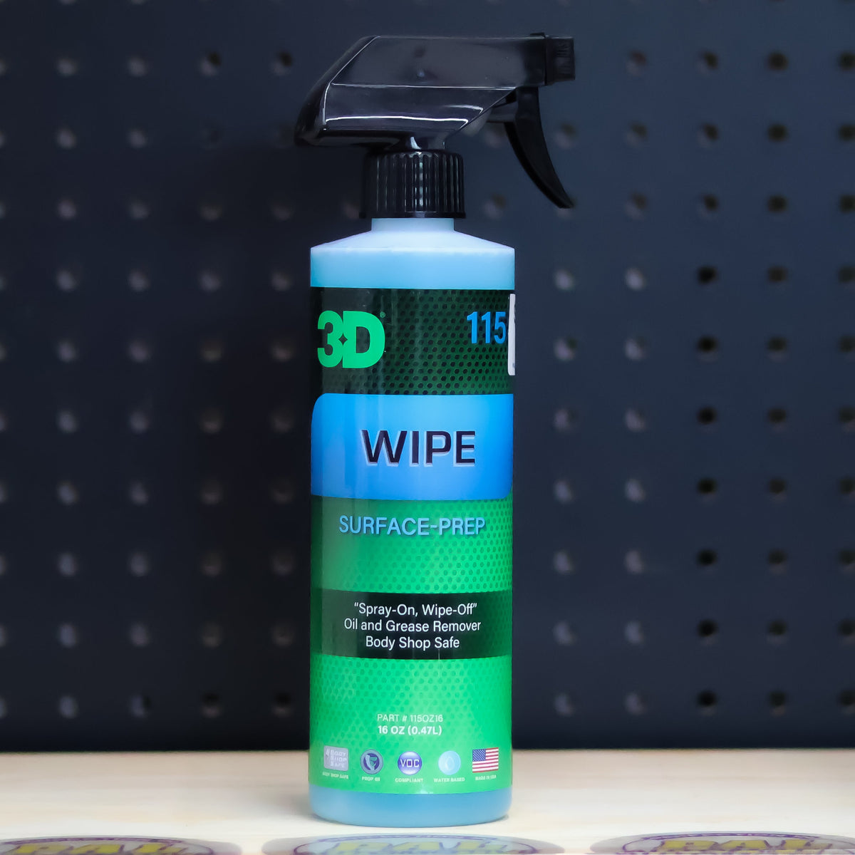 3D Wipe surface prep pint bottle, green and blue label with a black trigger sprayer, on a bench in front of a dark pegboard